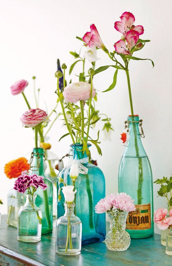 Bouteilles en verre transparentes vertes et bleues utilisées comme soliflore avec des fleurs variées et colorées